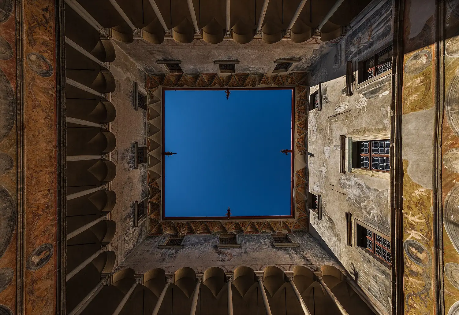 Il cortile di Palazzo Besta visto dal basso: il loggiato affrescato incornicia un quadrato di cielo blu